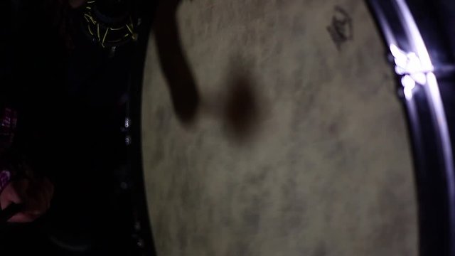A man playing a large drum in a dark room, close up.
