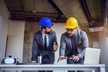 Two dedicated hardworking architects standing in building in construction process and working on improvement of blueprints.