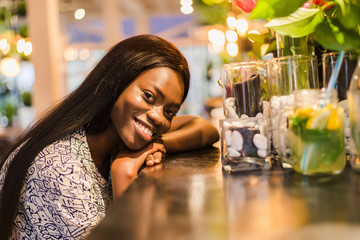 African woman in a modern cafe. Young african female sitting at a cafe counter having lemonade.