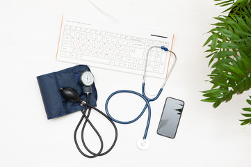 Top view of the doctor's workplace. Tonometer, stethoscope, phone and keyboard on wooden background.