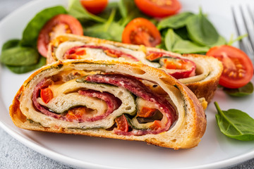 Italian food Pizza roll stromboli with cheese, salami, spinach and red pepper a light background.