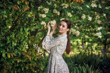 Beautiful young woman in a light summer dress at the flowering plants