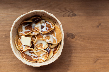 Fototapeta na wymiar Tiny pancake cereal quarantined trending food. Fun pastry at home for breakfast with sauce and butter on a plate. Grilled homemade food on a wooden table background. Mini Top view place for text