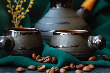 coffee beans are scattered on the table. Two cups of coffee stand on a black background. Green fabric decor, Turk and mimosa branch
