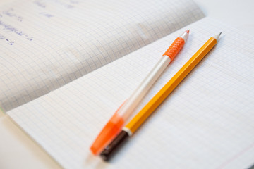 Educational tools. Orange pen and yellow pencil lie on on a notebook in a cage. Office and school tools.