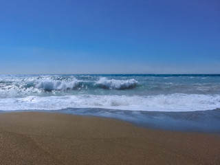 Fototapeta na wymiar Blue stormy sea with blue sky and dark sand.