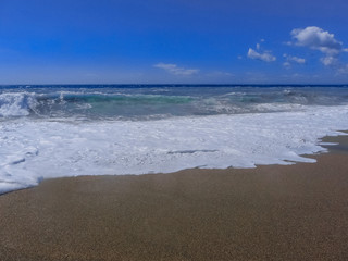 Blue stormy sea with blue sky and dark sand.