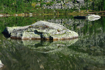 Fototapeta na wymiar Large textured stone in a mountain lake