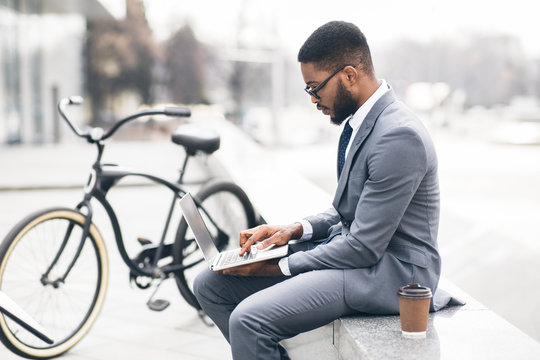 Handsome manager working on laptop sitting on parapet