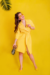 girl with a pineapple on a yellow background. Girl in a yellow raincoat on a yellow background