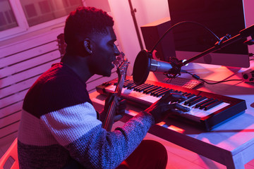African american professional musician recording synthesizer in digital studio at home, music production technology concept.