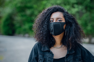 Portrait of a young girl in a black mask on the street. Green background. Space for text.
Health,...