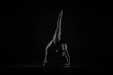 Girl yogi performs exercises on a black background. The flexibility of the female body. Asana. Relief of the muscles. Figures from the body.