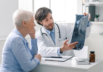 Doctor showing x-ray scans of head to senior female patient