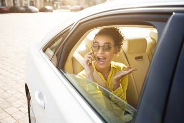 Joyful African Lady Talking On Mobile Phone Sitting In Car