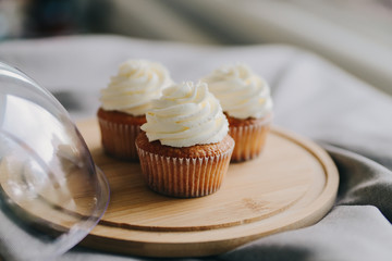 Three classic cupcakes with buttercream on a round wooden Board.