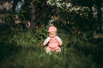 Little child sitting on lawn in park in pink clothes under the open sky