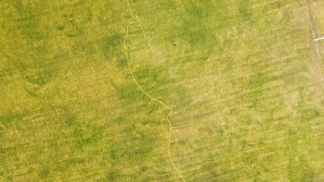 Top down aerial view of football field surface covered with green grass and sprinklers spraying water.