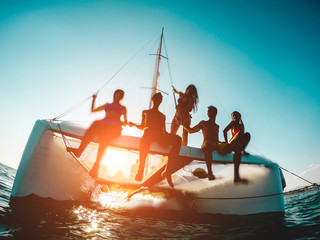 Silhouette of young friends chilling in private catamaran boat - Group of people making sea tour trip - Alternative travel vacation during Coronavirus outbreak - Focus on left girl - Water on camera - obrazy, fototapety, plakaty