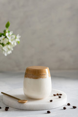 Trendy dalgona coffee in a glass with whipped foam on gray background with coffee beans. Iced whipped coffee, korean coffee concept. Side view, copy space
