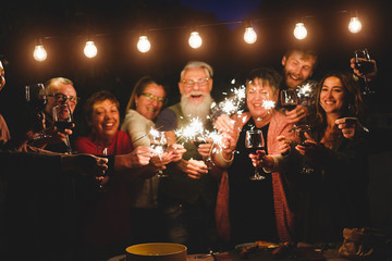 Happy family and friends celebrating with sparkler fireworks at home dinner - Different age of people having fun together in patio party - Celebration and summer holidays concept - Focus on left hands