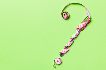 Fototapeta premium Top view of question mark made of fork and measuring tape on green background. Diet concept with copy space