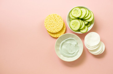 Facial clay mask in bowl and care items on a pink background