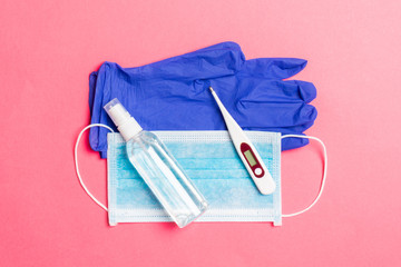 Top view of alcohol hand sanitizer, latex gloves, digital thermometer and medical mask on pink background. Virus protection equipment concept with copy space