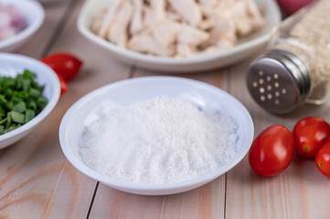 Salt in a white spoon, tomatoes placed on a wooden table.