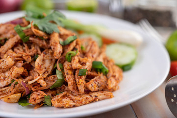 Spicy minced chicken on a white plate complete with cucumber, lettuce and side dishes.