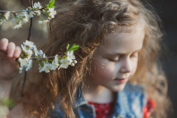 Naklejka premium Cute little girl with curly hair in a flowering garden