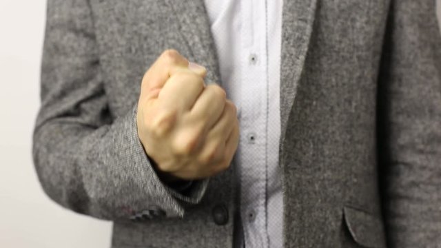 Solid caucasian man in gray jacket and speckled shirt on white background pulling fist up. close-up on male fist shaking in front of camera. threat gesture, concept of aggression, warning, punishment