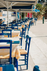 Romantic Greek restaurant with blue chairs and tables under palm leaves, Greece