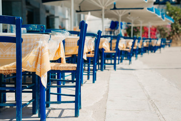 Romantic Greek restaurant with blue chairs and tables under palm leaves, Greece