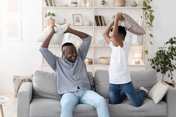 Fun With Grandpa. Cheerful Black Grandfather Pillow Fighting With Grandson At Home