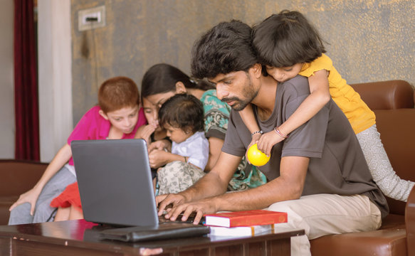 Children Or Kid Playing By Riding On Father Back And Disturbing While Father Busy In Working On Laptop - Concept Of Work From Home Or WFH During Covid-19 Or Coronavirus Pandemic.