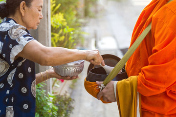An old Asian woman is offering food to Buddhist monks at in front home in the morning, to offer...