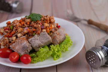 Spicy pork minced with tomatoes and lettuce on a white plate on a wooden table.