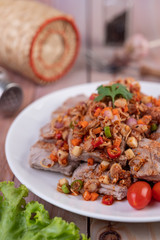 Spicy pork minced with tomatoes and lettuce on a white plate on a wooden table.