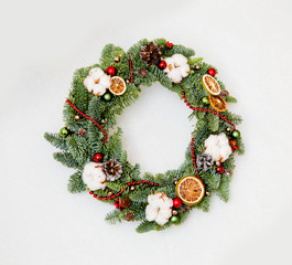 Christmas wreath with red shiny beads with flowers of cotton and slices of dried oranges
