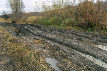 Fototapeta premium An impassable road, off-road track in autumn forest. Deep ruts in the slushy autumn road