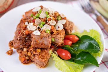 Spicy pork minced with tomatoes and lettuce on a white plate on a wooden table.
