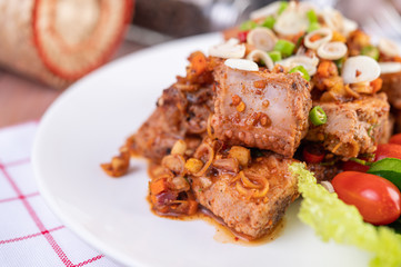 Spicy pork minced with tomatoes and lettuce on a white plate on a wooden table.