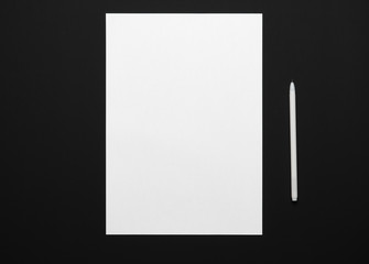 a blank sheet of paper and a pen on a black table, top view - template for any text or inscription