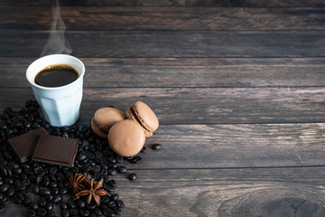 Wooden background with steaming coffee, coffee beans, chocolate, macarons and star anise.