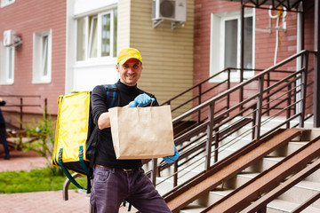 Young courier with thermo bag near the house. Food delivery service