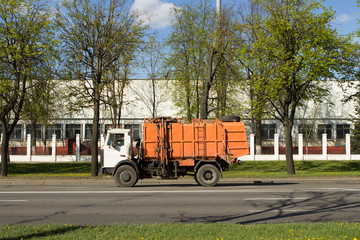 An orange garbage truck rides along a city street