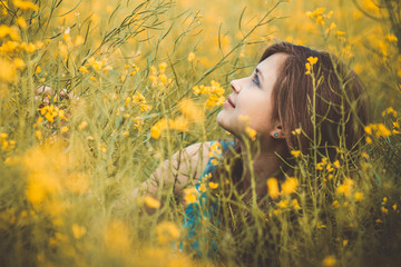 beautiful romantic girl sitting on blooming rapeseed field enjoying nature, young elegant woman walking, pretty female face looking up from flowers