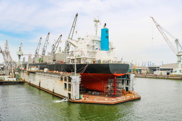 Fototapeta premium Cargo ship moored at floating dry dock under repair in shipyard.