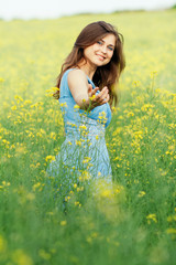 Naklejka na ściany i meble beautiful romantic girl on blooming rapeseed field enjoying nature, young elegant woman holds out hand calling for walk in the field